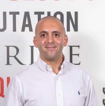 InTouchnow Joins Primary Care Accelerator to Scale AI Voice Reception for UK GP Practices Smiling, bald man in a white button-down shirt posing in front of a backdrop with large letters.