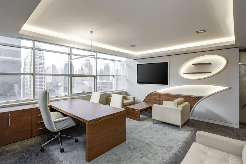 Modern high-rise office with wooden desks, white chairs, and a curved wall feature overlooking a city skyline through large windows.