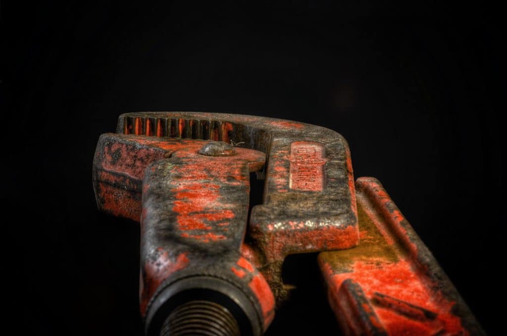 How Hiring a Local Plumber Transforms Your Home Repairs? Close-up of a weathered red-orange rusted vise or clamp with jagged jaws against a dark background.