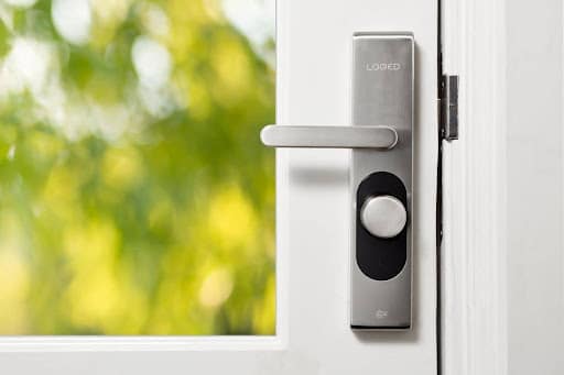 How to keep uPVC doors working all year round Close-up of a silver door handle and electronic lock on a white door, with a blurred green garden outside.