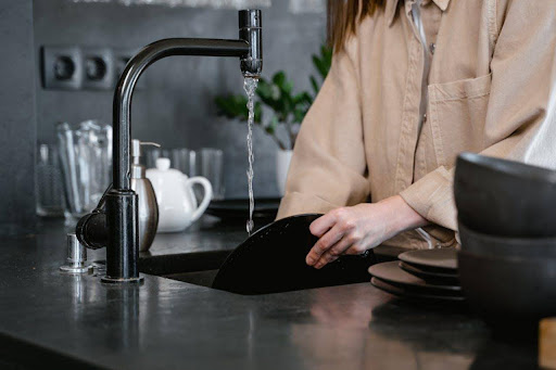 From snaking to jetwashing: What’s the best way to unclog drains? Person rinsing a black plate under a running faucet at a modern kitchen sink.