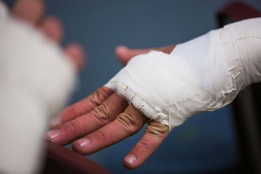 Close-up of a hand wrapped in a white medical bandage, with fingers exposed and a blurred background.