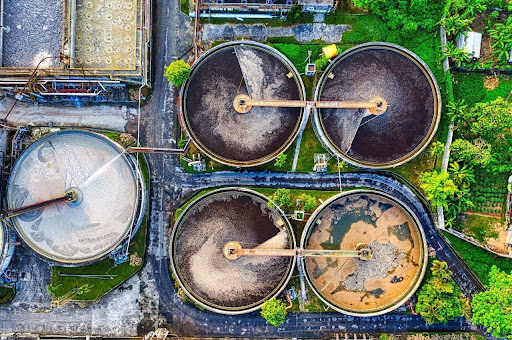 Wastewater surveillance made simple with qPCR kits Aerial view of a wastewater treatment plant with four circular clarifier tanks and surrounding greenery.