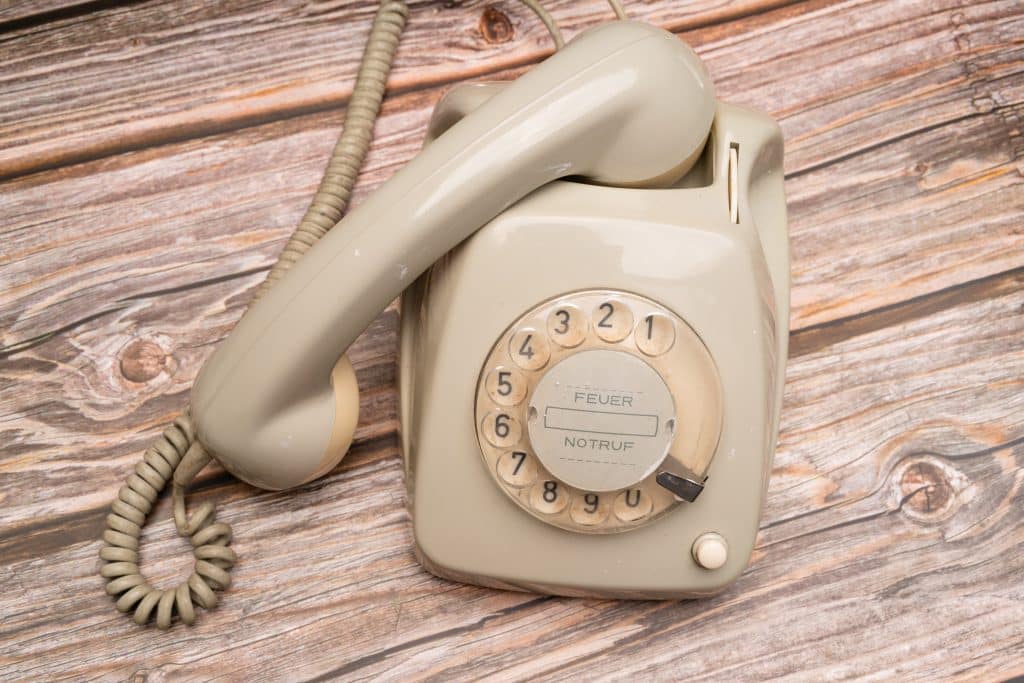 Cloud Telephony vs Landlines: Why It’s Time to Upgrade Beige vintage rotary telephone on a weathered wooden tabletop with a coiled cord visible at the side.