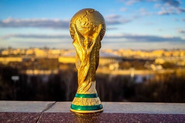 The oldest players ever to appear at a World Cup FIFA World Cup Trophy, gold statue with globe on top, held by sculpted arms, on a ledge with a cityscape in the background