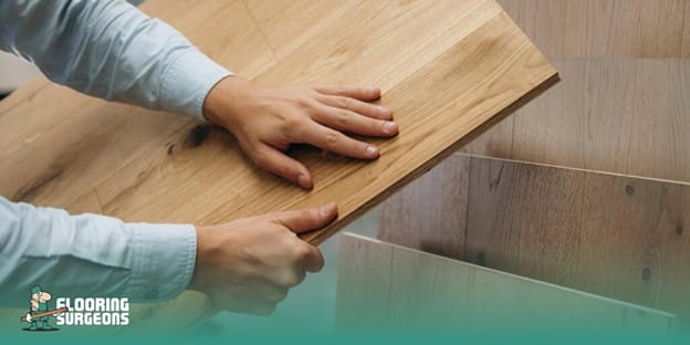 Confused Between LVT & LVP? Read This First! Hands fitting a wooden flooring plank during installation, with the Flooring Surgeons logo in the corner.