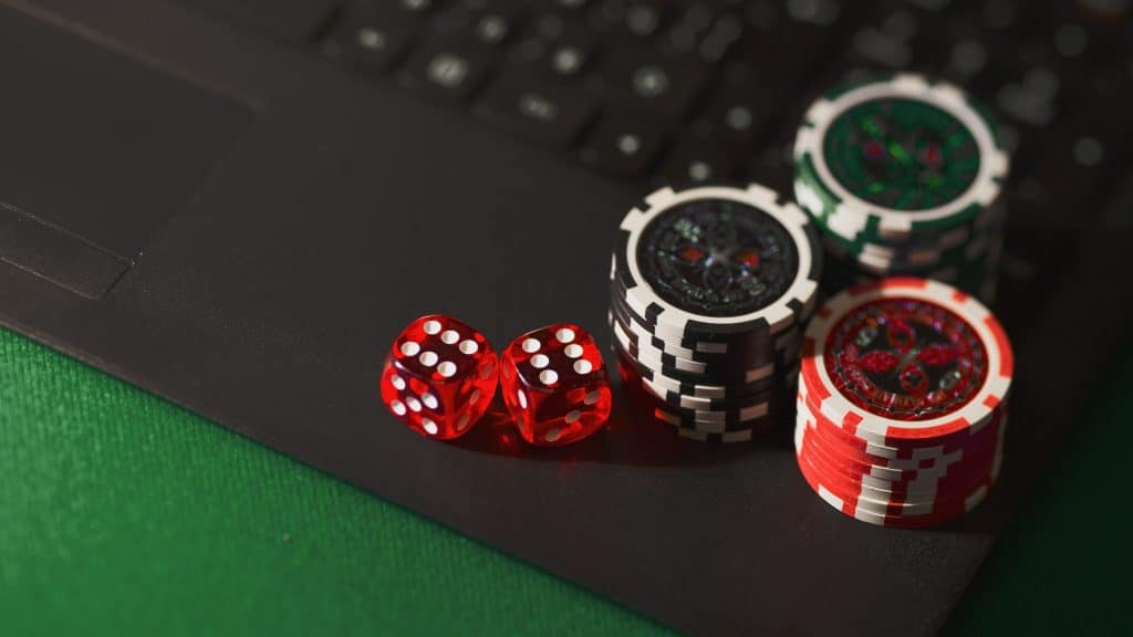 How Casinos Have Changed Over the Last Decade Red dice and stacked poker chips sit on a green casino table with a blurred laptop in the background.