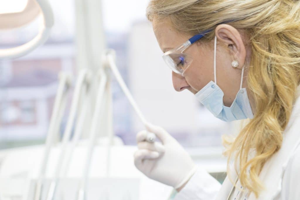 3 Best Cosmetic Dentists in London for a Wedding-Ready Smile Scientist wearing safety goggles and mask, examining samples at a lab bench from a side view