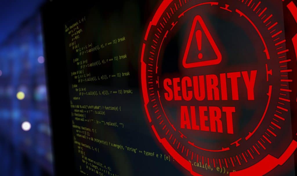 How Organisations Are Reducing Exposure to Advanced Cyber Risks Red security alert badge over a dark screen with green code lines, signaling a cybersecurity warning