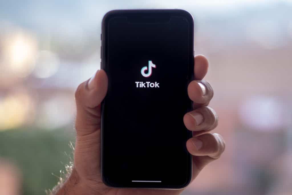 Hand holding a smartphone showing the TikTok logo on the screen, centered on dark display.