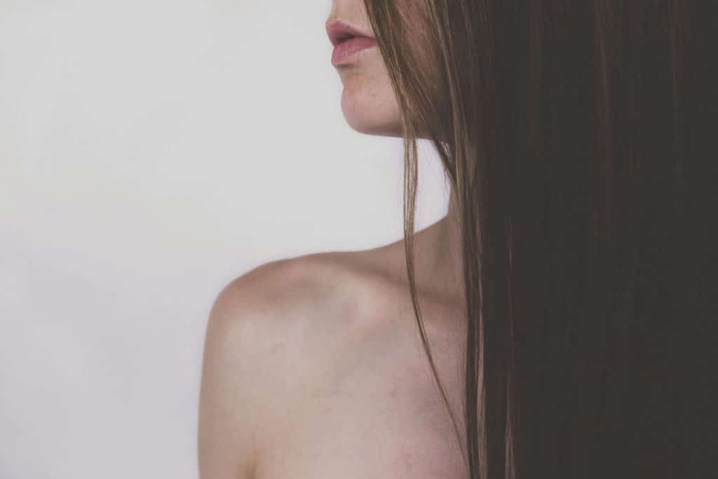Why Smooth and Soft Hair Is Highly Valued in Extensions Close-up side profile of a woman's face with long dark hair partially covering her features, bare shoulder visible.