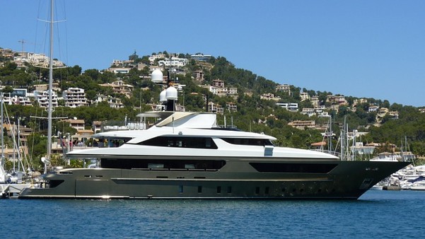 Large luxury motor yacht anchored in a marina with hillside houses in the background.