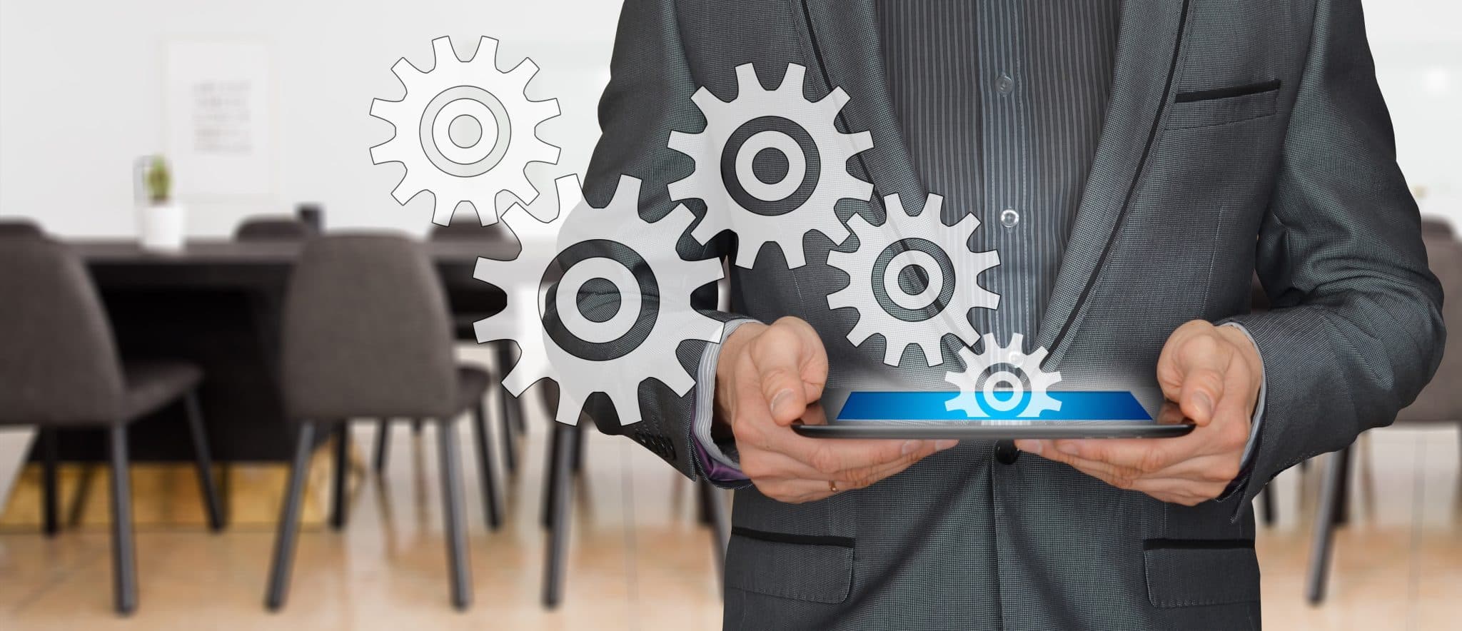 Business professional in a suit uses a tablet with gear icons floating around, symbolizing automation in business workflows, blue highlight on tablet screen