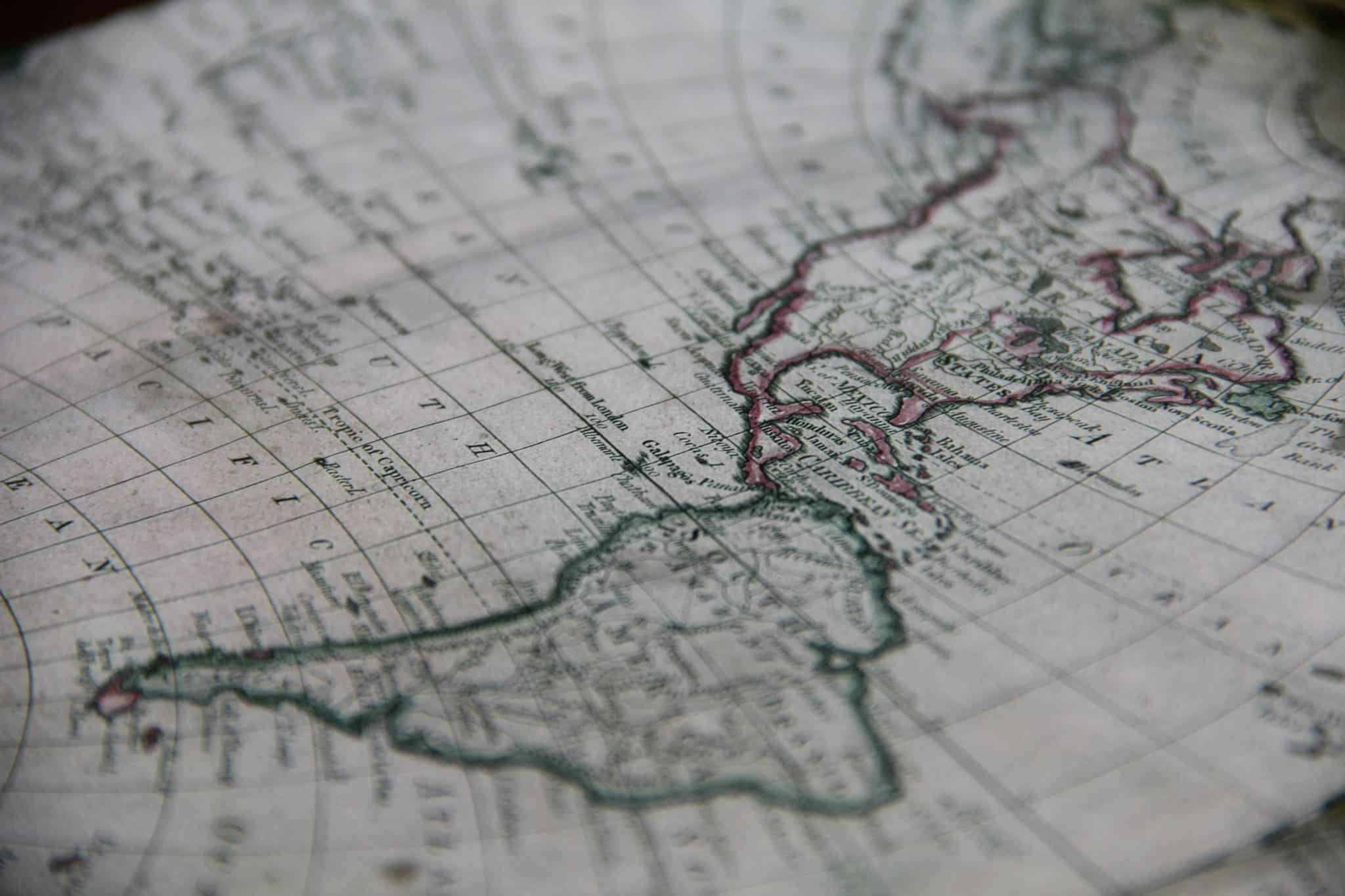 Close-up of an antique map showing a coastline outlined in pink with grid lines and small place names into view.