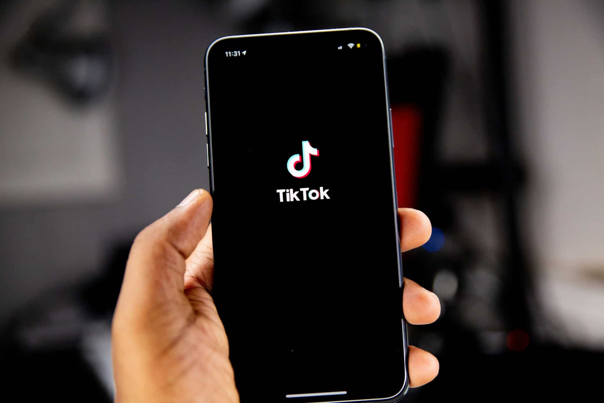 Hand holding a smartphone showing the TikTok logo on the screen with a black background.