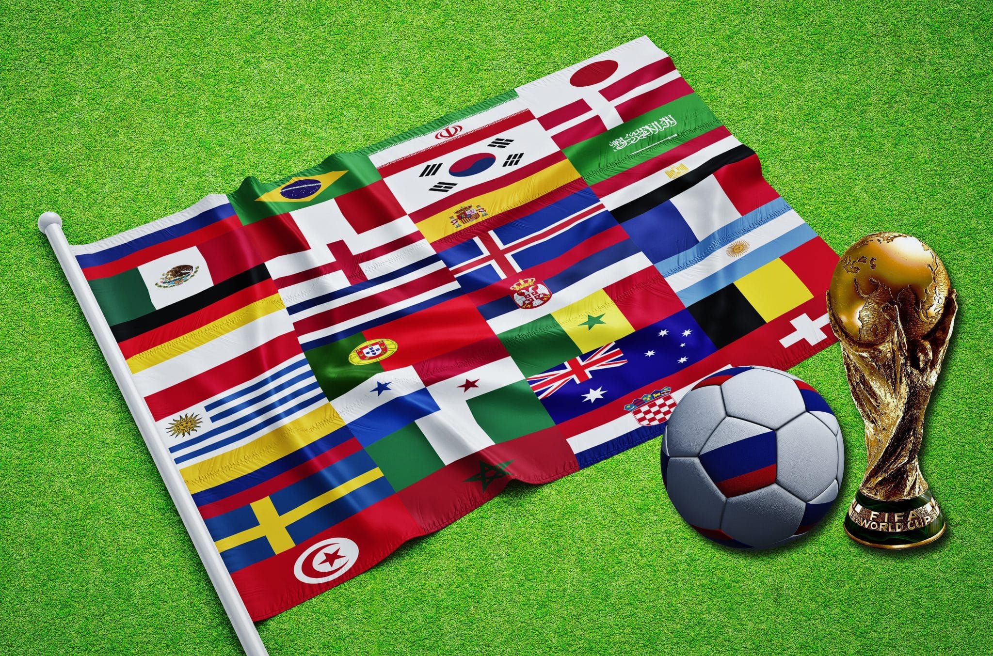 Flag banner with many countries laid on a soccer field beside a soccer ball and FIFA World Cup trophy on green grass