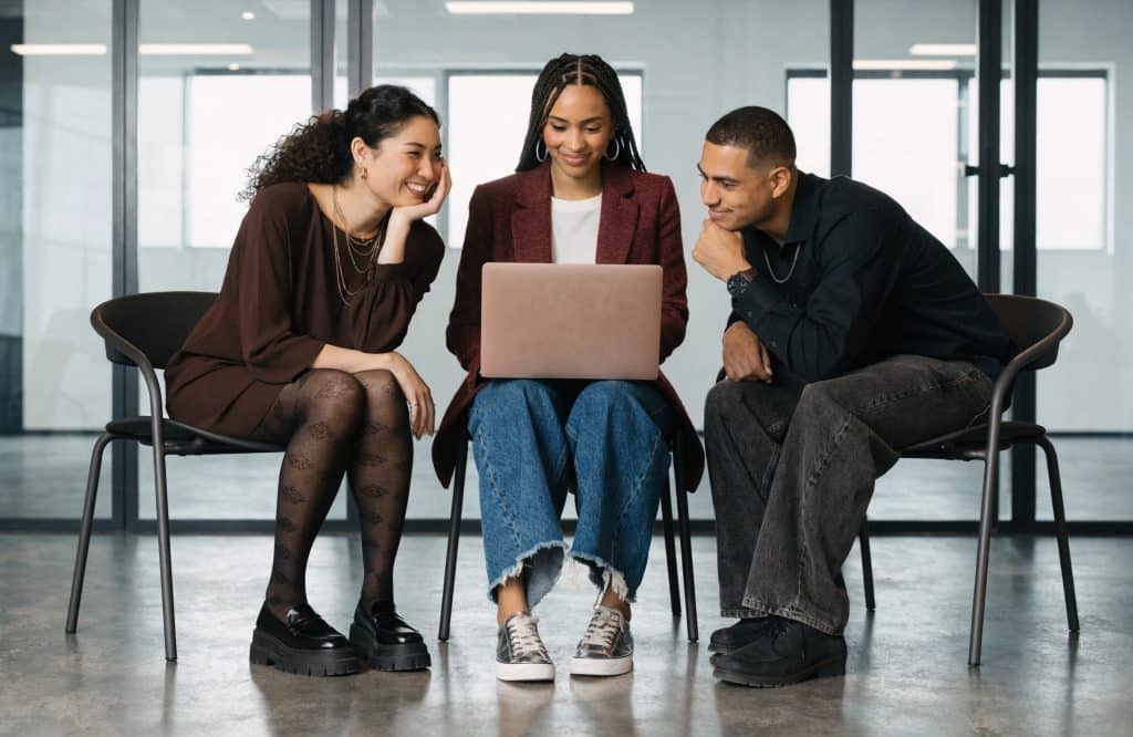 How to build strong professional networks as a small firm Three coworkers sit together, looking at a laptop and smiling in a modern office.