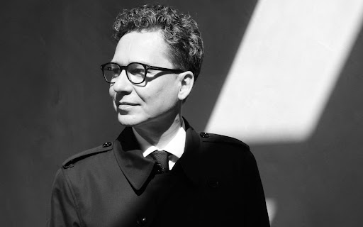 Black-and-white portrait of a man wearing glasses, a dark coat and tie, looking to the right.
