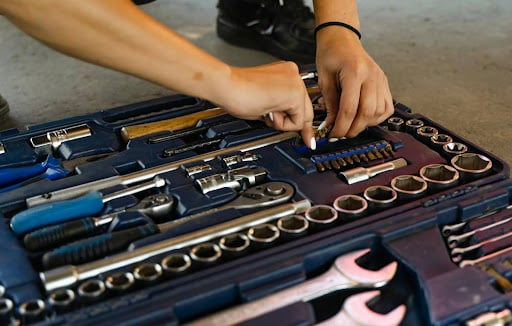 Hands reach into an open toolbox, organizing sockets, wrenches, and bits on a blue case.