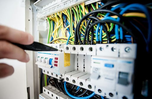 Technician using a screwdriver to adjust a circuit breaker panel with colorful wires.