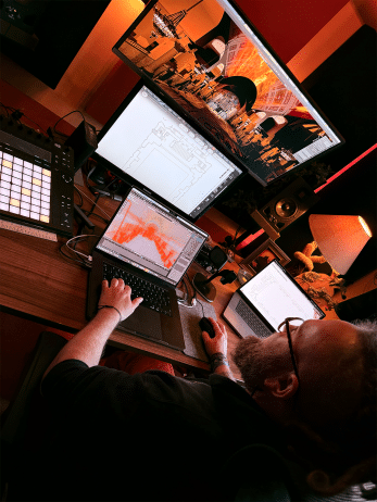 05- Behind the Scenes Creating the Sky | OTS News - Southport Designer at a multi-monitor workstation editing architectural drawings with a laptop, tablet, and large screen in a red-lit studio setting.