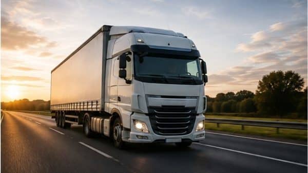 White semi-truck with trailer driving on a highway at sunset.