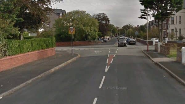 Residential street with a yield sign ahead as the road narrows, cars parked along the curb in a quiet neighbourhood.
