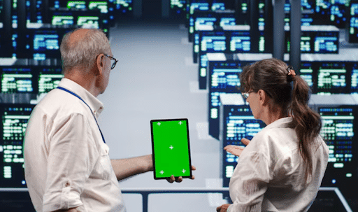 Two professionals in a data center examine a tablet with a green screen between them.